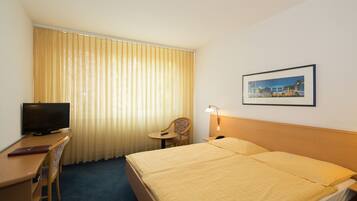 Habitación de hotel con cama, escritorio con televisor, silla, mesita y lámpara de pared.