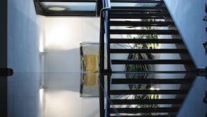 Un intérieur moderne avec un ascenseur en verre, un escalier doté de rampes en métal et une plante en arrière-plan.