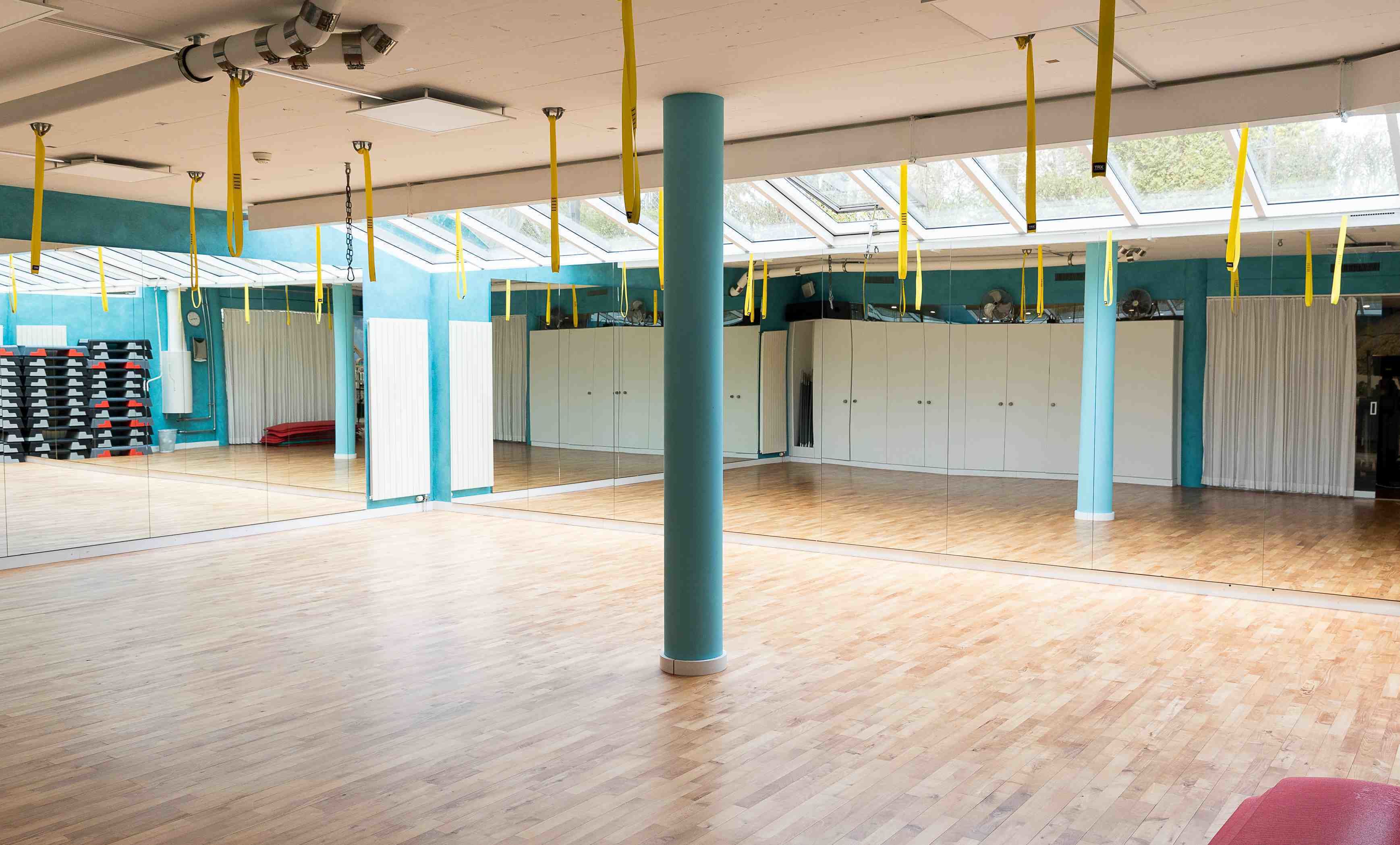 Une pièce spacieuse dotée d’un plancher en bois, d’une grande fenêtre et de sangles de suspension jaunes.