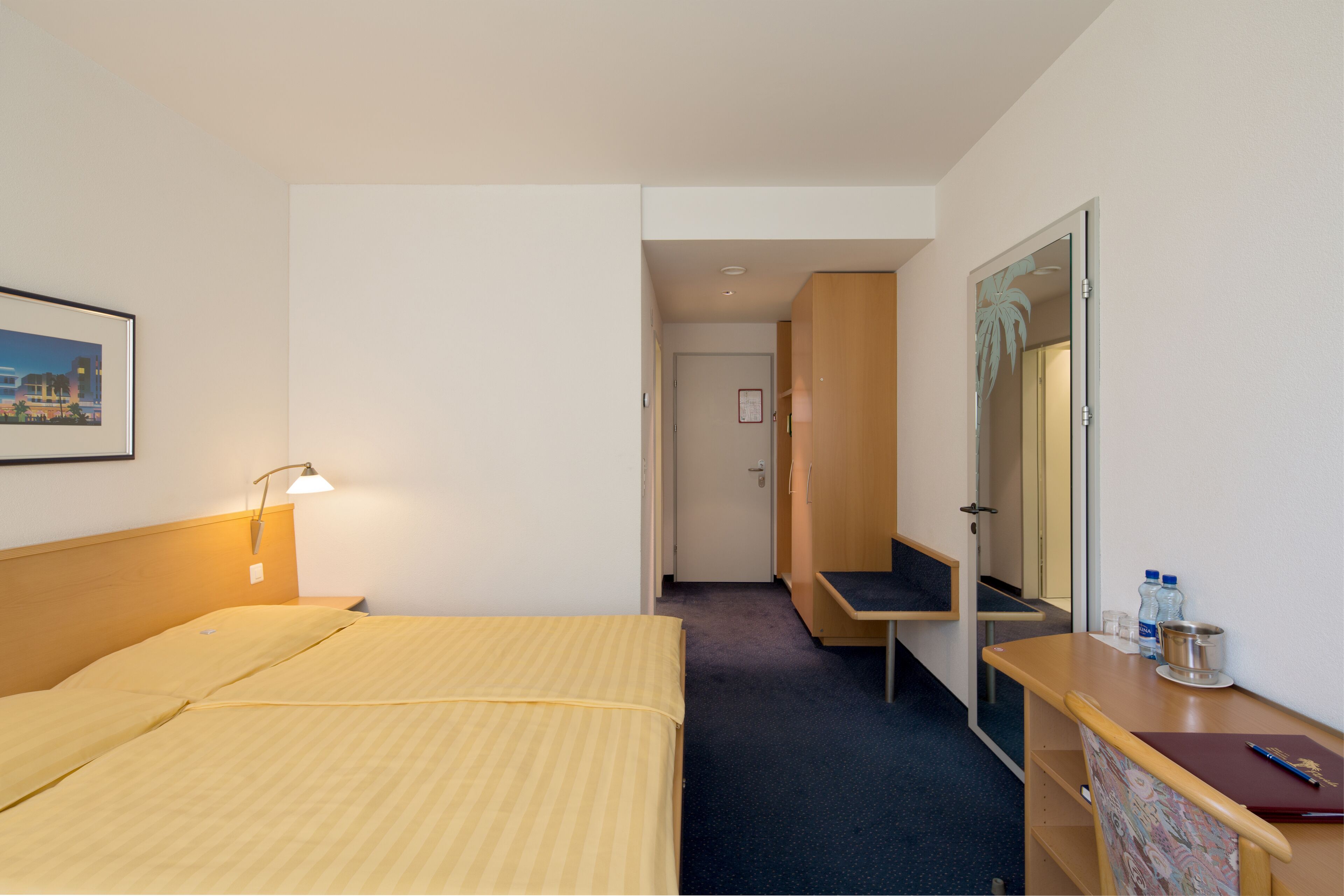 A hotel room with a bed, bedside lamp, desk, chair, and a mirror.