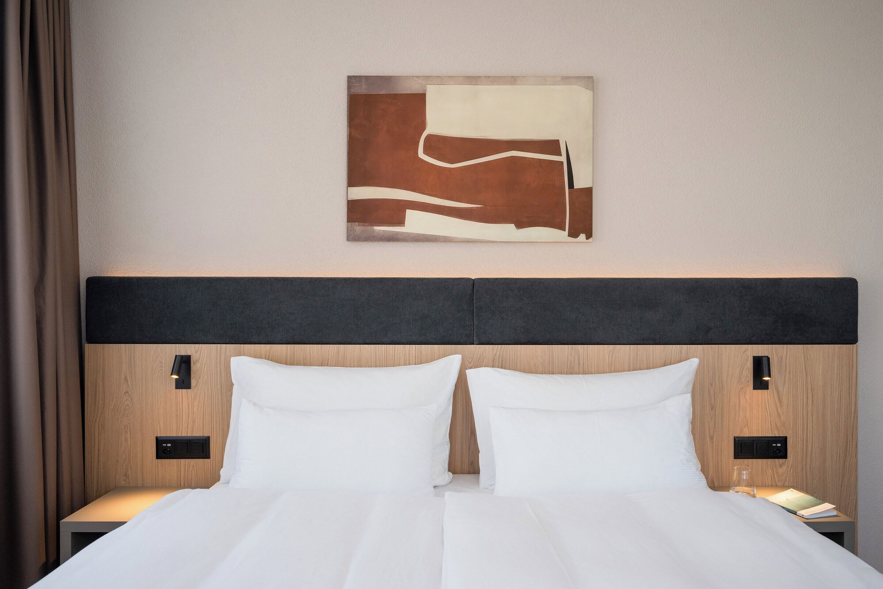 Une chambre d’hôtel comprenant un lit, deux tables de chevet, une œuvre d’art accrochée au mur et une tête de lit dotée d’un éclairage intégré.