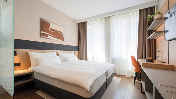 A hotel room with a bed, desk, chair, and a TV. - Tailormade Hotel METROPOL St.Gallen (St. Gallen)