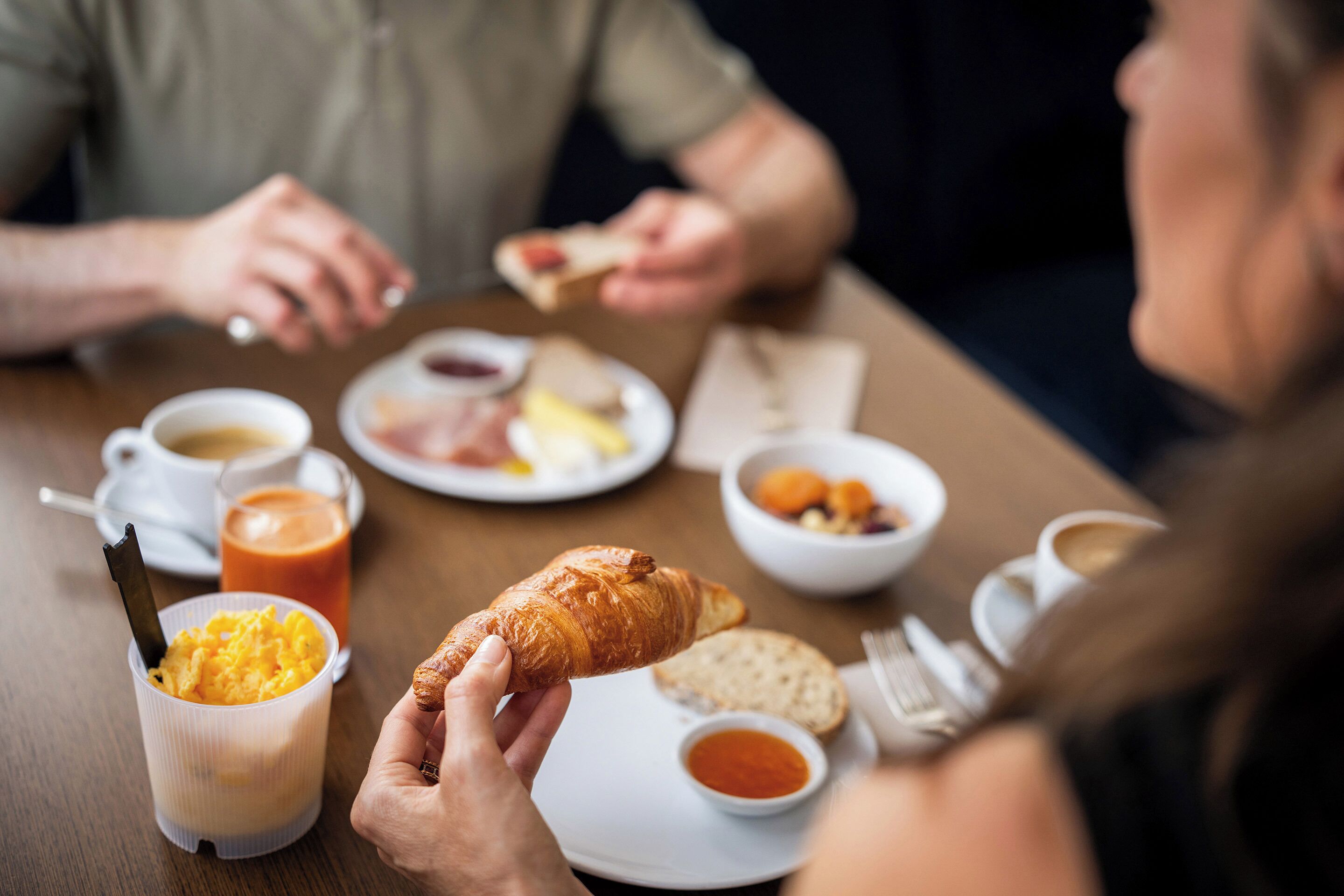 A dining table with various food items and beverages, including a croissant, bread, and coffee.