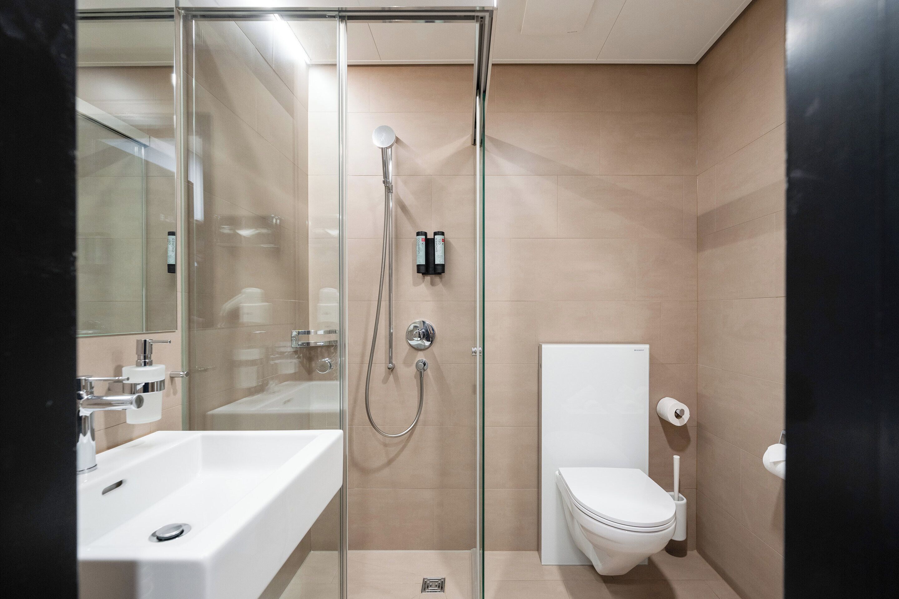 Un baño moderno con ducha de vidrio, lavamanos blanco y un inodoro.