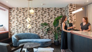 A reception area with a patterned wall, a blue sofa, a marble table, and a potted plant. - Tailormade Hotel METROPOL St.Gallen (St. Gallen)