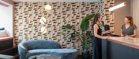 Zona de recepción con pared decorativa, sofá azul, mesa de mármol y una planta en maceta.