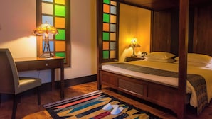 Un lit à baldaquin avec un cadre en bois et une table de chevet avec une lampe. Un bureau avec une chaise et une lampe est placé à côté du lit.