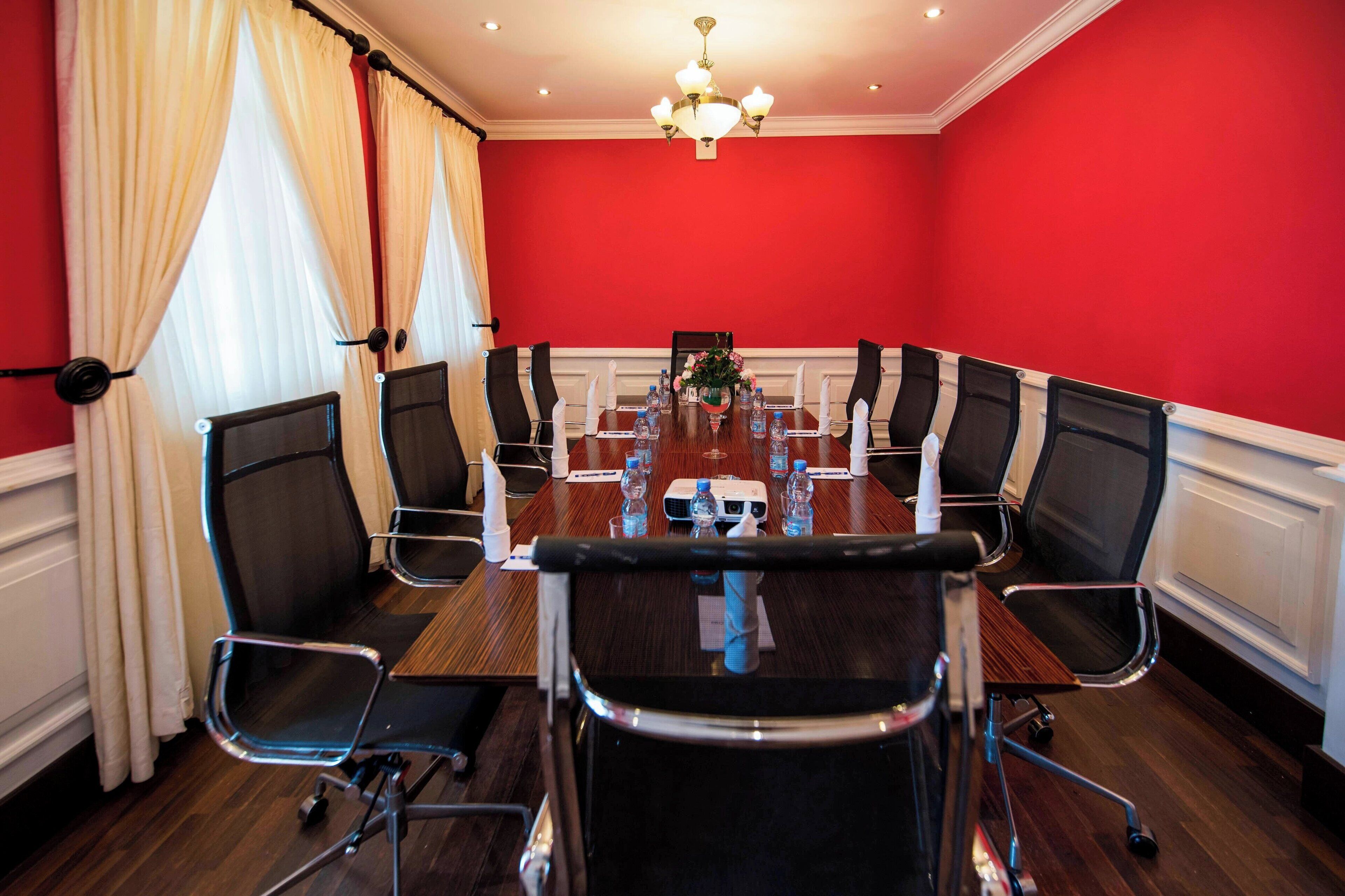 Un salón de conferencias con una larga mesa, sillas negras y un candelabro.
