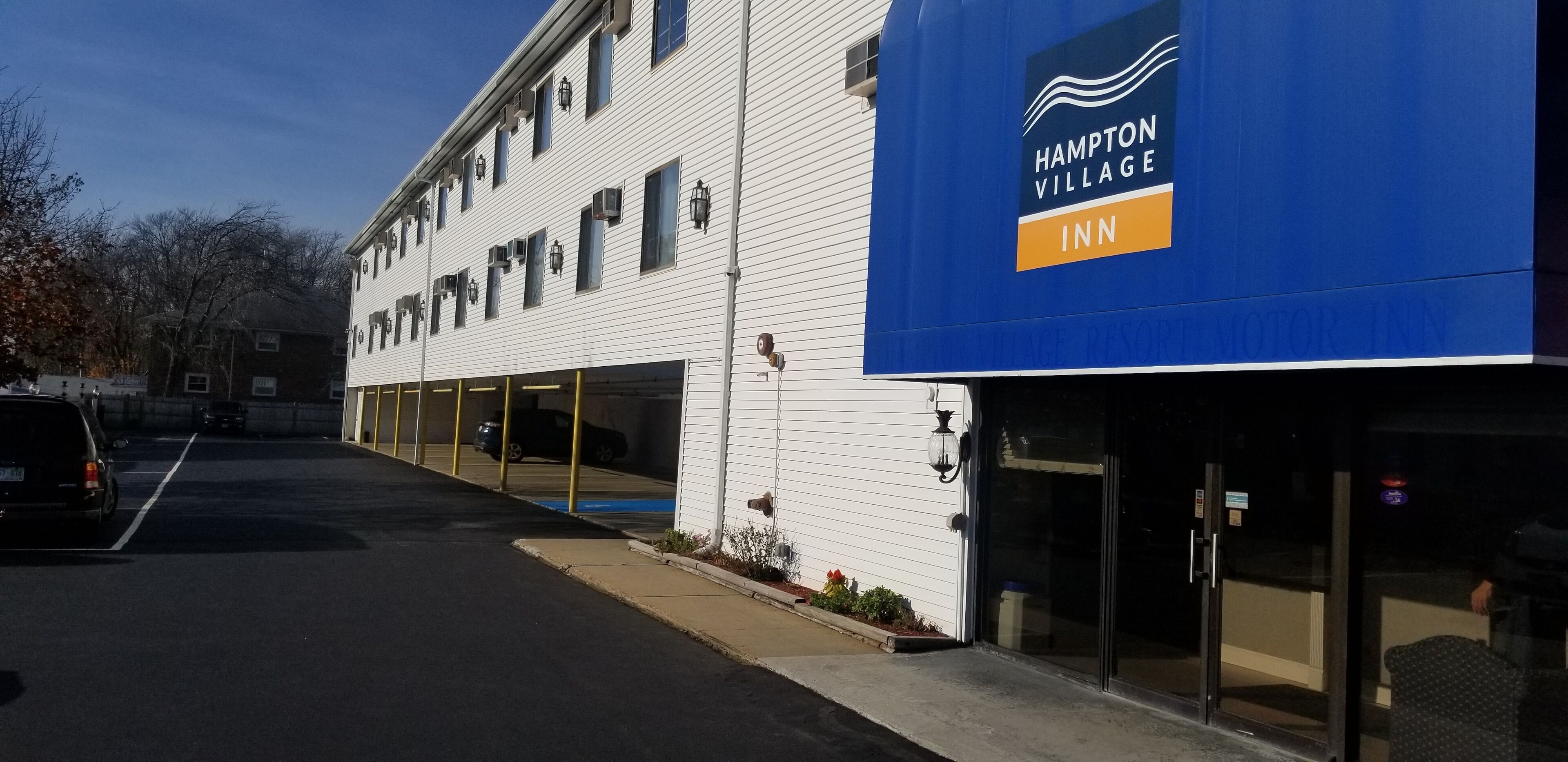 Edificio de Hampton Village Inn con toldo azul, estacionamiento y cielo despejado.