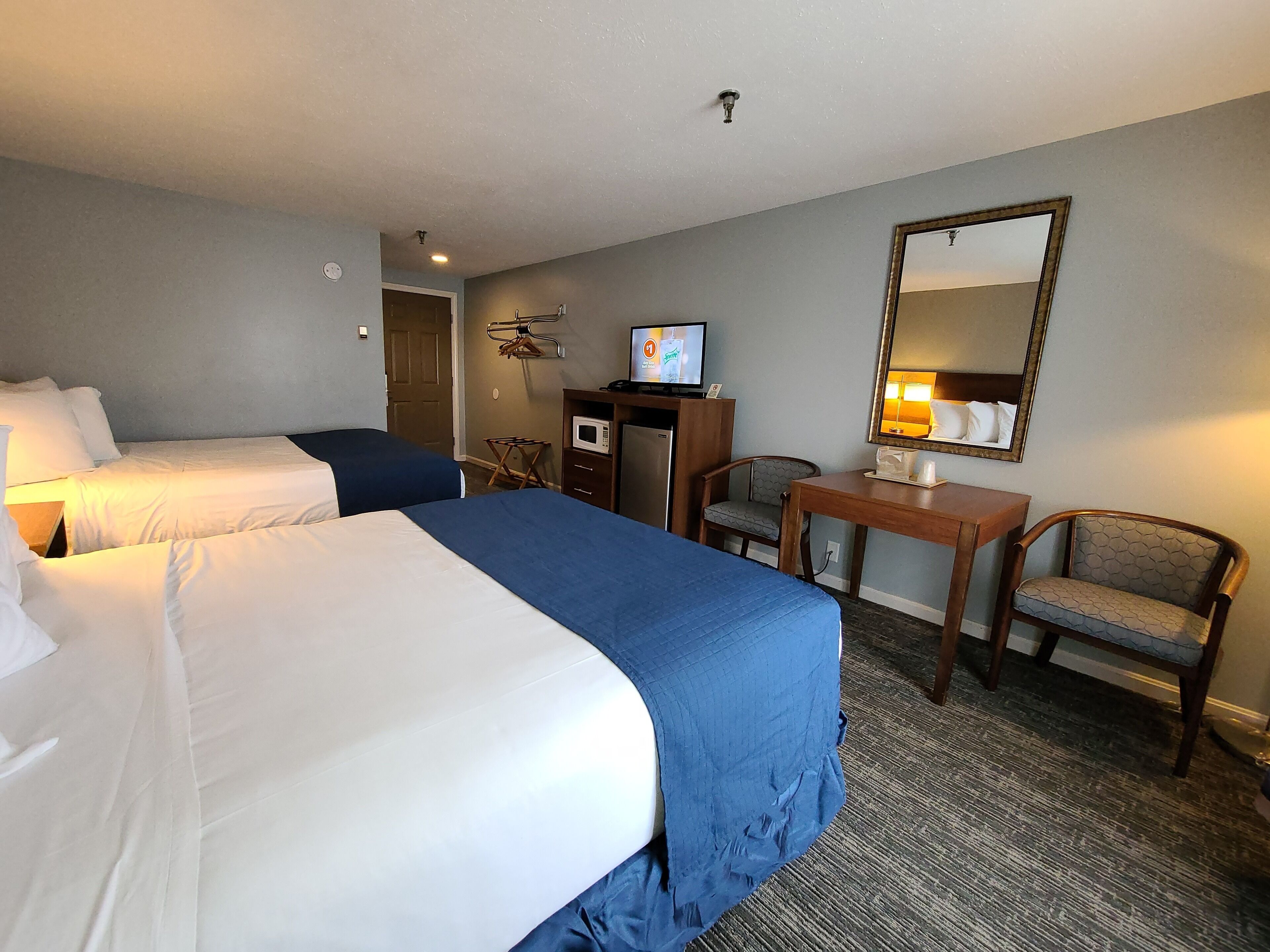 Une chambre d’hôtel avec deux lits, un bureau, une chaise, un four à micro-ondes et une télévision.