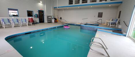 An indoor swimming pool with clear blue water, a lifeguard chair, and a pool ladder.