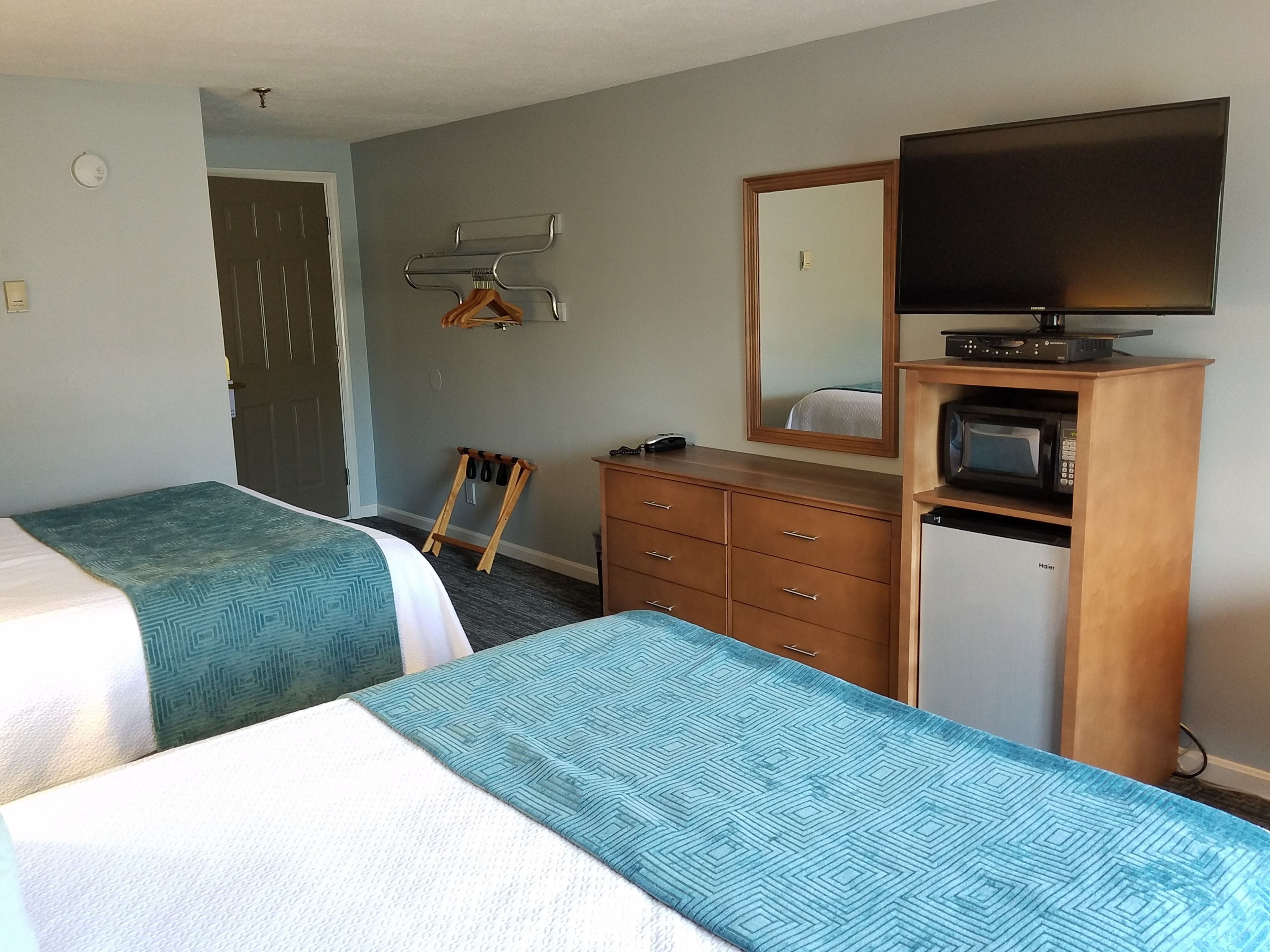 Habitación de hotel con dos camas individuales, un aparador de madera, un microondas, un televisor y un espejo.