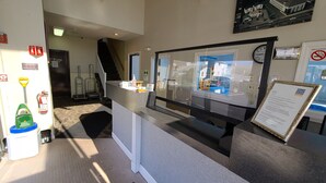 A reception desk with a glass partition, a clock, and a framed informational sign. - Hampton Village Inn (Hampton)