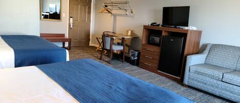 A hotel room with two beds, a desk, a television, and a sofa.