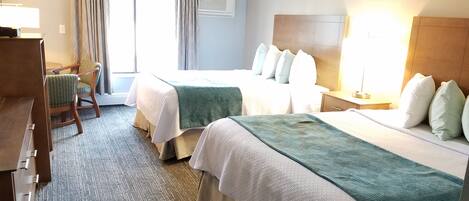 A hotel room with two beds, a desk, a chair, and a window with curtains.