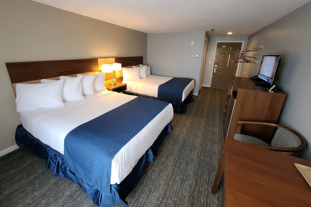 A hotel room with two beds, a desk with a computer, and a chair.
