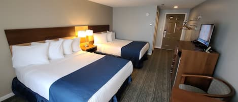 A hotel room with two beds, a desk with a computer, and a chair.