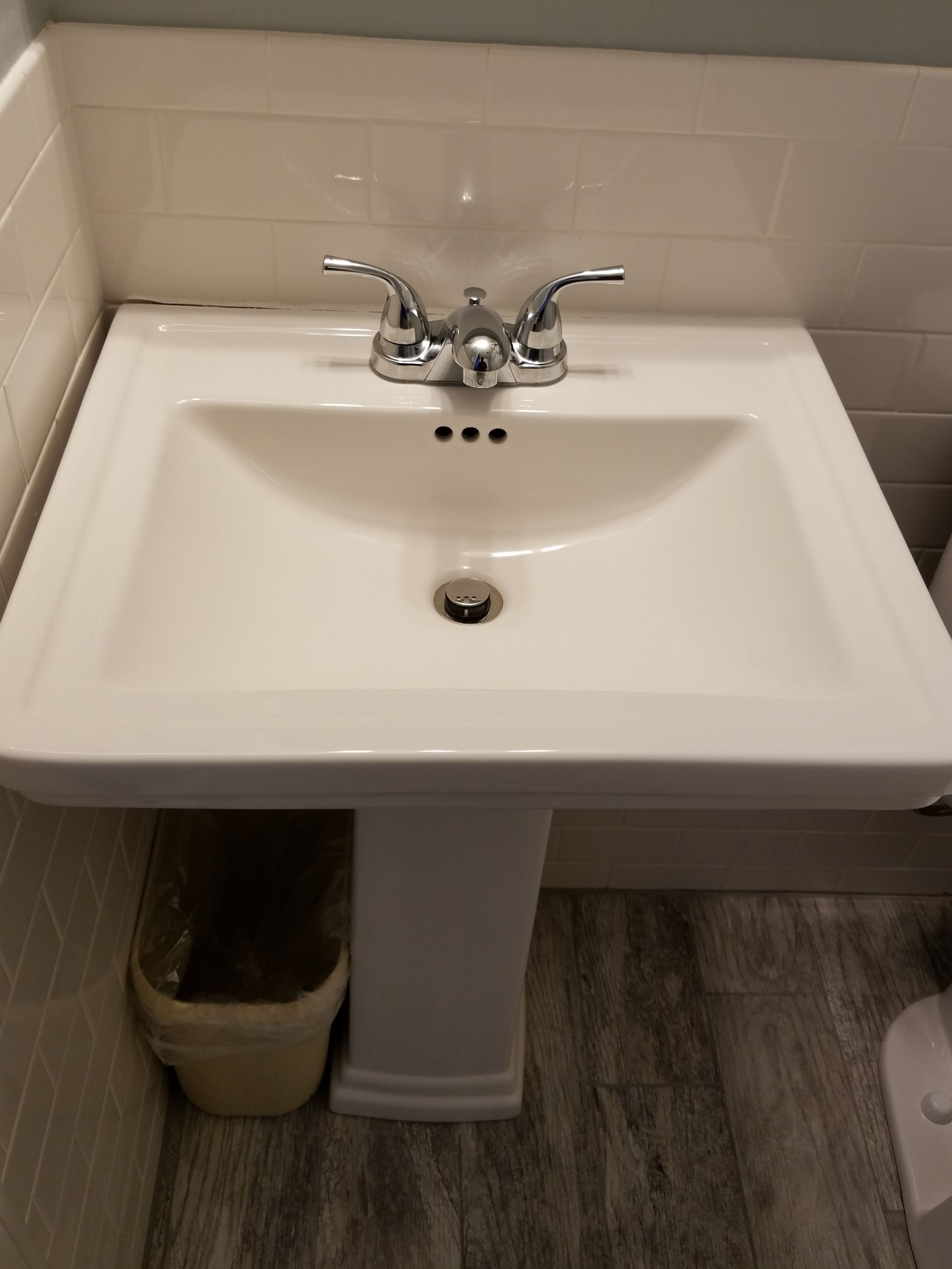 A bathroom sink with a white basin, two faucets, and a drain.