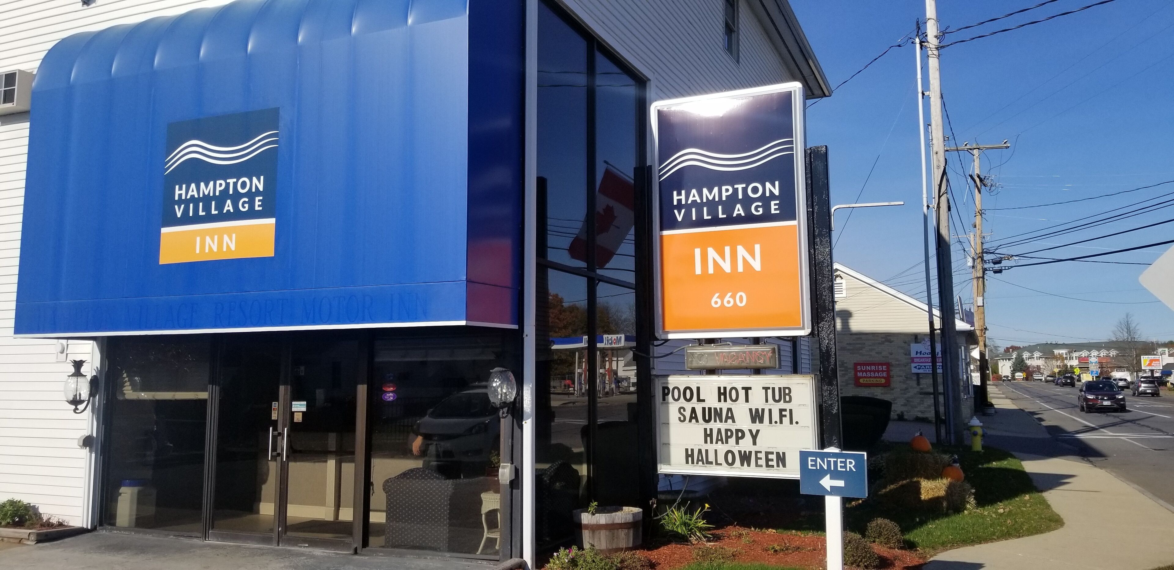 A Hampton Village Inn with a blue awning and a sign indicating amenities like a pool, hot tub, sauna, and Wi-Fi.