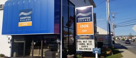 A Hampton Village Inn with a blue awning and a sign indicating amenities like a pool, hot tub, sauna, and Wi-Fi.