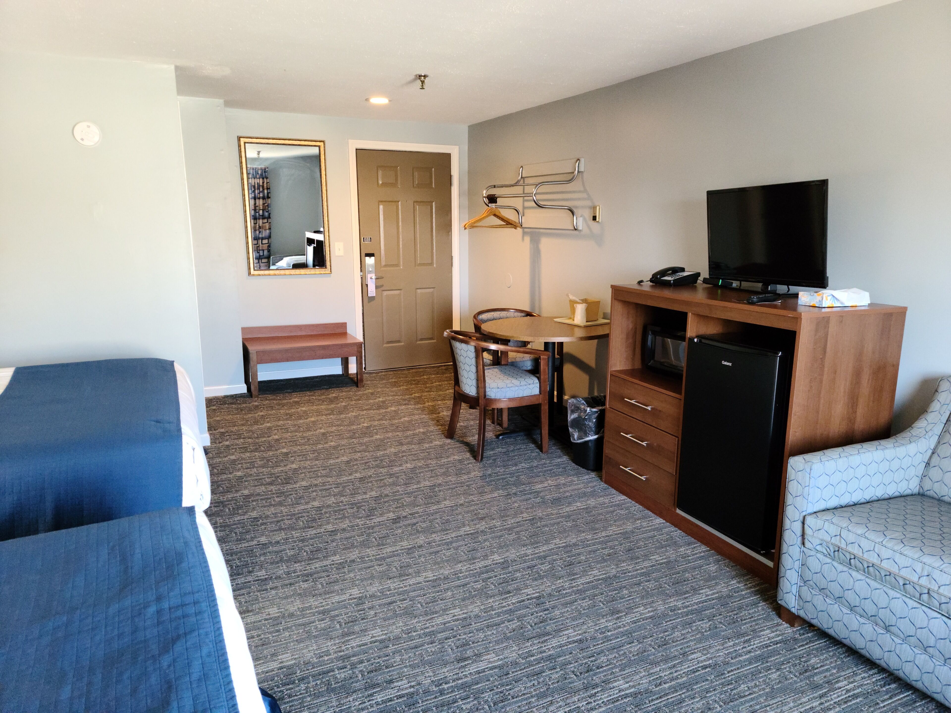 A hotel room with two single beds, a desk with a chair, a television, a microwave, and a small refrigerator.