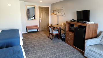A hotel room with two single beds, a desk with a chair, a television, a microwave, and a small refrigerator.