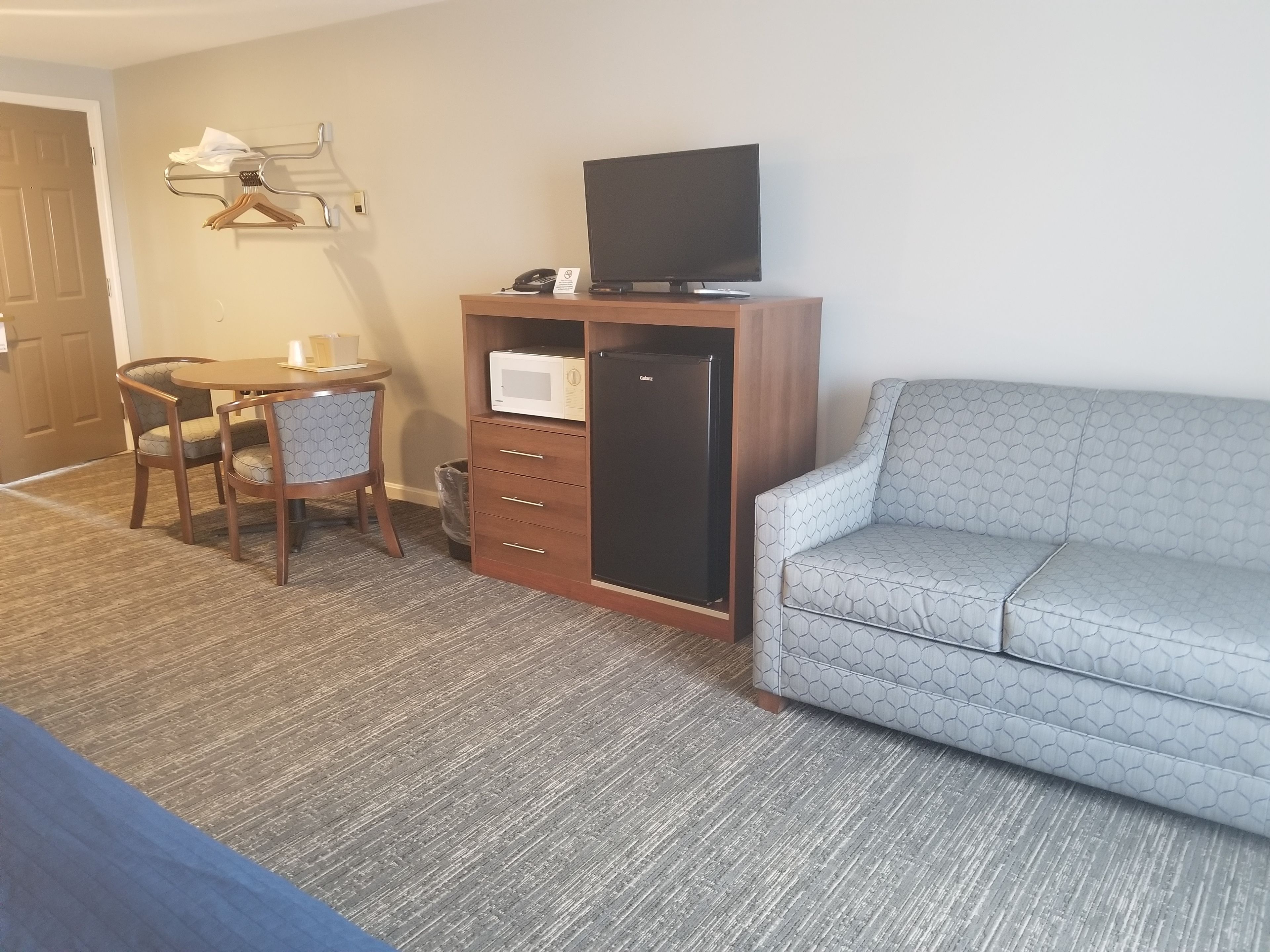 A hotel room with a sofa, a small table with chairs, a microwave, a refrigerator, and a television.