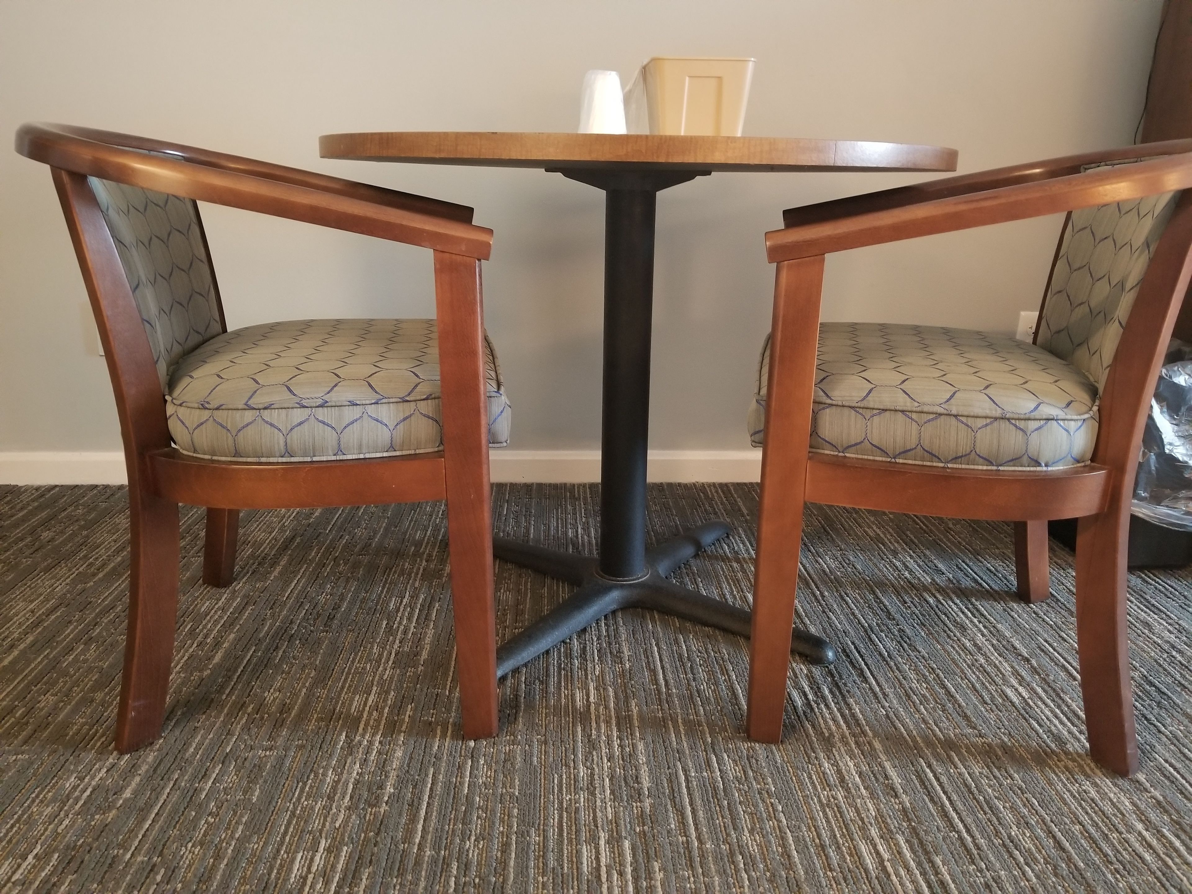 A round wooden table with a black base, flanked by two chairs with patterned cushions.