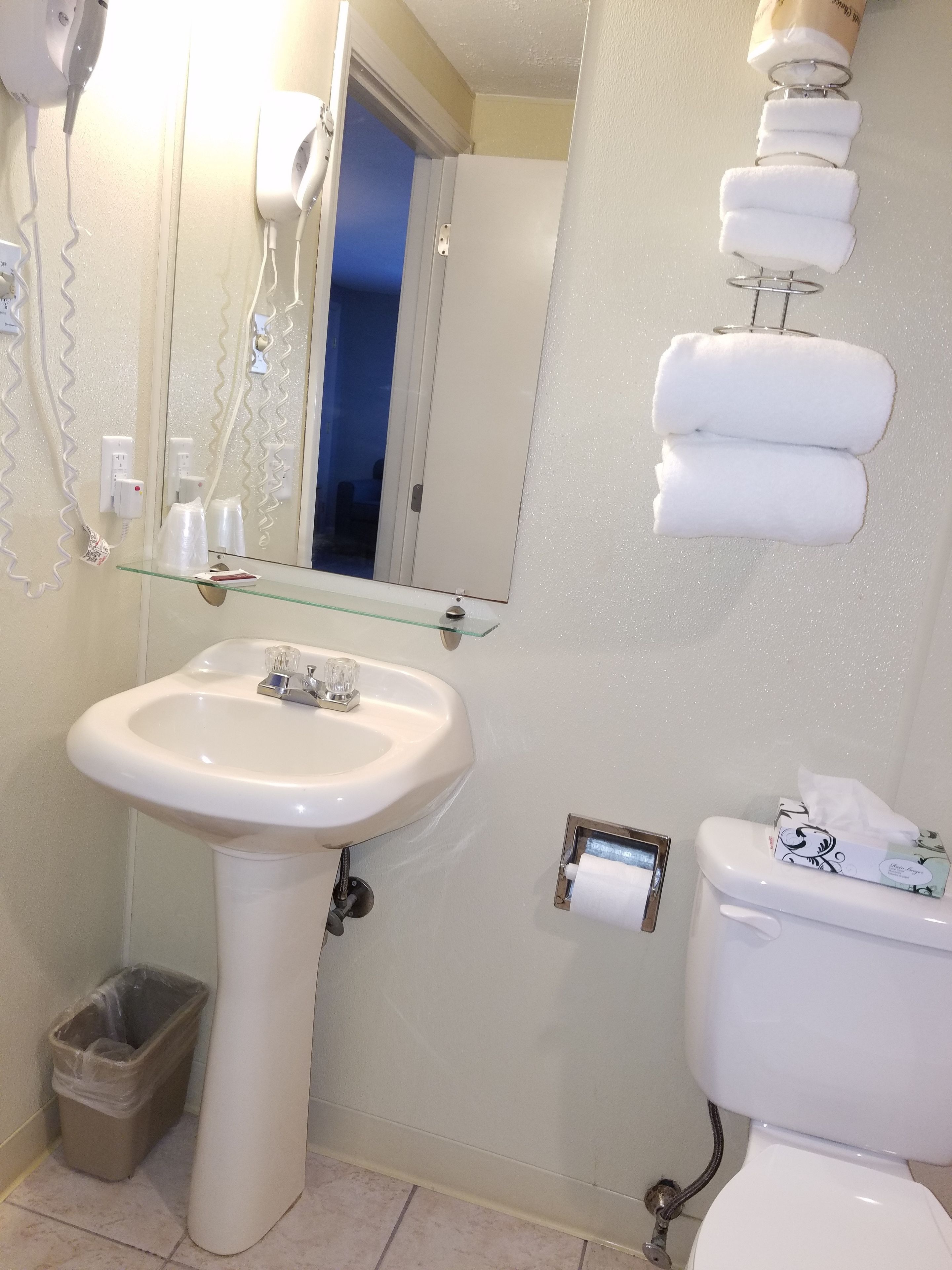 A bathroom with a white sink, a toilet, and a glass shelf.