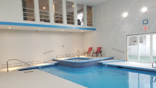 An indoor swimming pool with a blue tiled edge, a small hot tub, and two red chairs. - Hampton Village Inn (Hampton)