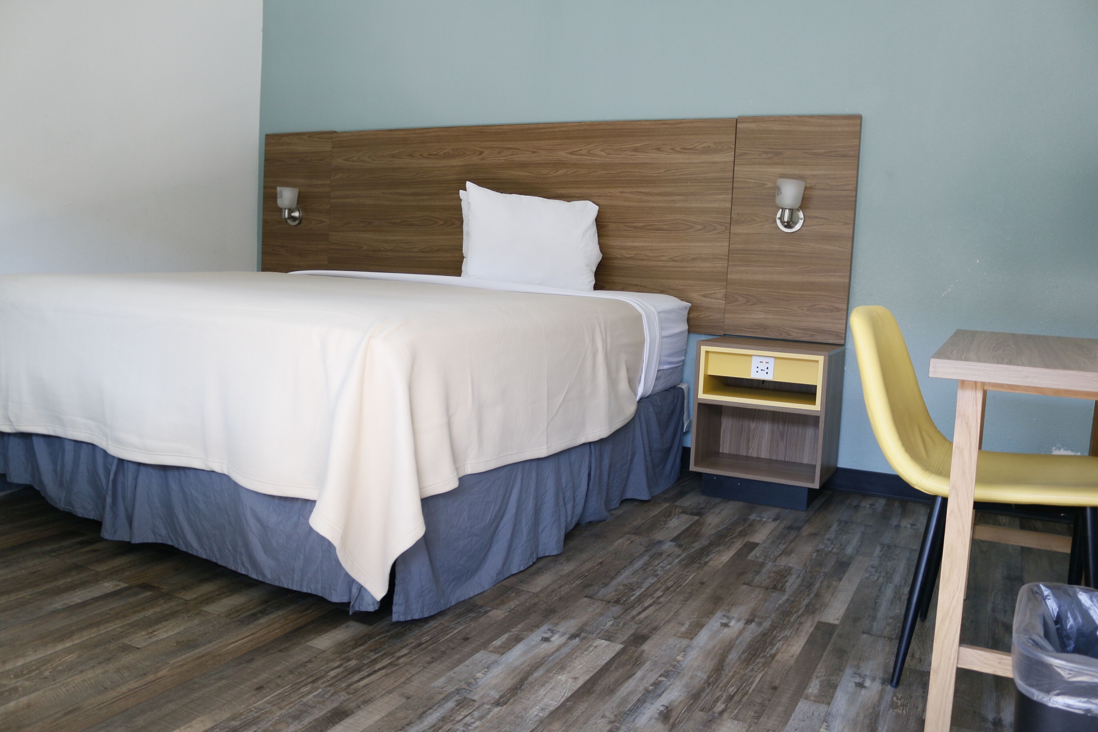 A neatly made bed with a wooden headboard, a bedside table with a lamp, and a yellow chair.