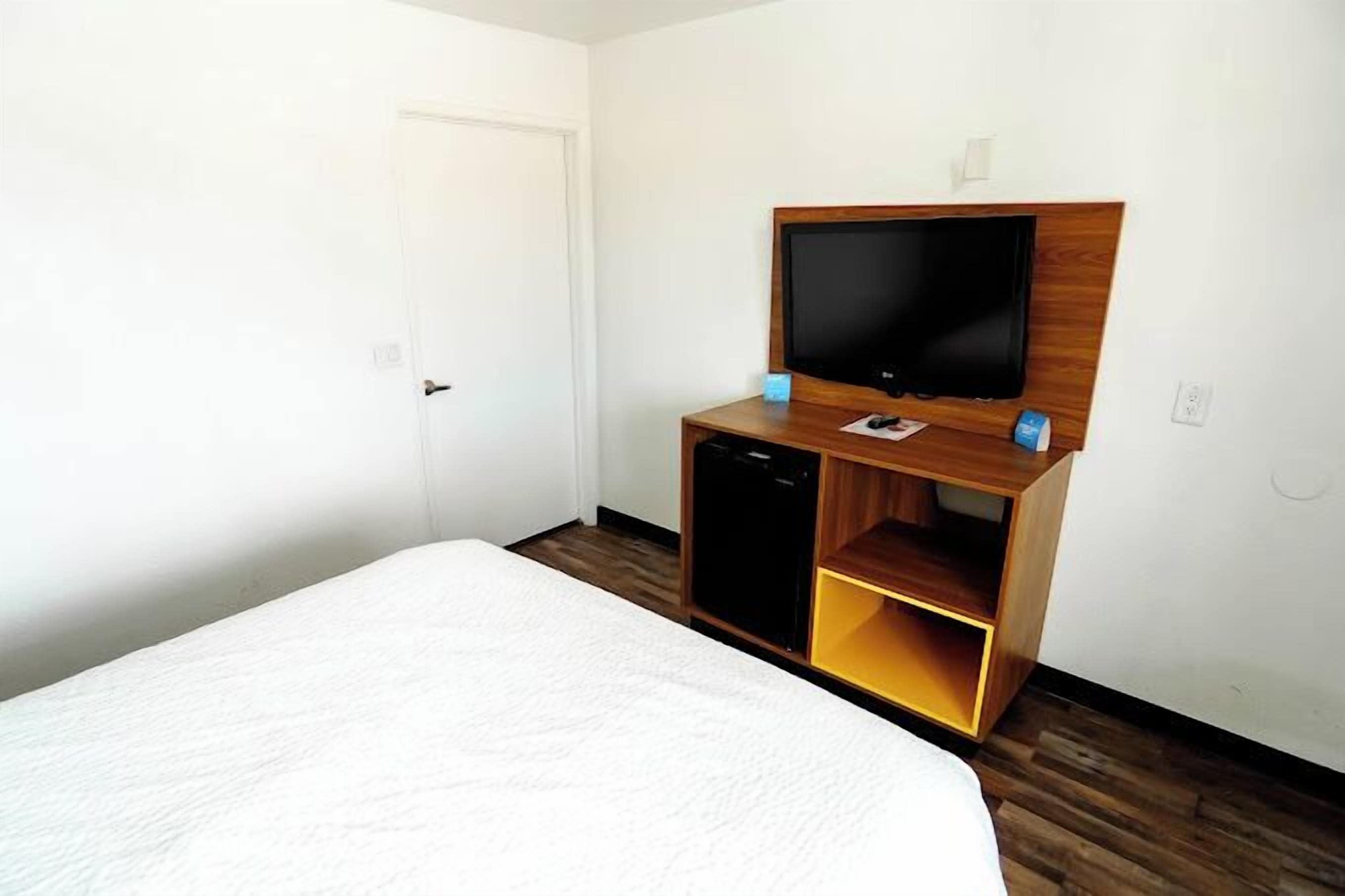 A hotel room with a bed, a TV on a wooden stand, and a door.