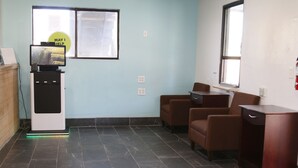 Ein Zimmer mit Schreibtisch, zwei Stühlen, einem kleinen Tisch, einem Automaten und einem Fenster.