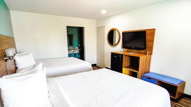 Ein Hotelzimmer mit zwei Betten, einem Fernseher, einem Spiegel und einem kleinen Schreibtisch.