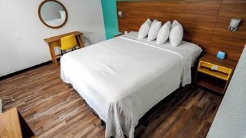 Habitació d'hotel ben ordenada amb un llit de fusta, un escriptori amb cadira i un mirall rodó a la paret.