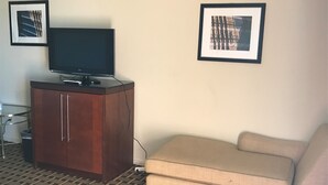 Uma sala de estar com uma TV sobre um móvel de madeira, um sofá bege e duas fotos emolduradas na parede.