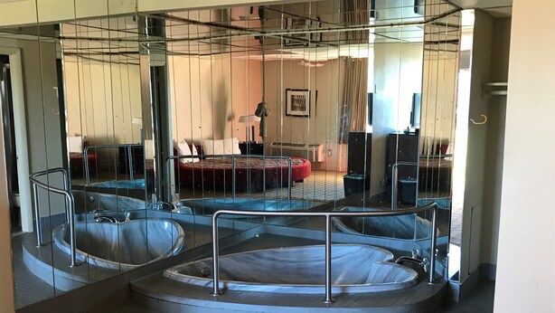 Área de spa com três banheiras de hidromassagem, uma cadeira vermelha e um espelho refletindo o ambiente.