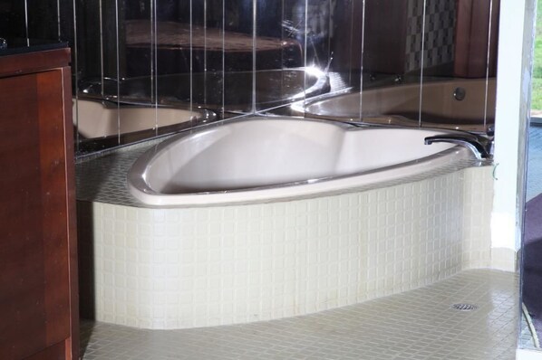 A corner bathtub with a curved design, a wooden cabinet to the left, and a tiled wall.