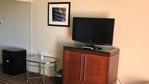 Quarto com televisão de tela plana sobre um aparador de madeira, uma mesa de vidro, um cesto de lixo e um tapete estampado.