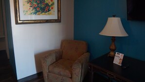 A room with a floral armchair, a table with a lamp, and a framed painting on the wall. - La Hacienda Hotel (Laredo)