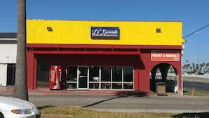 A building with a yellow and red facade, a Coca-Cola sign, and a sign indicating a low weekly and monthly rate. - La Hacienda Hotel (Laredo)