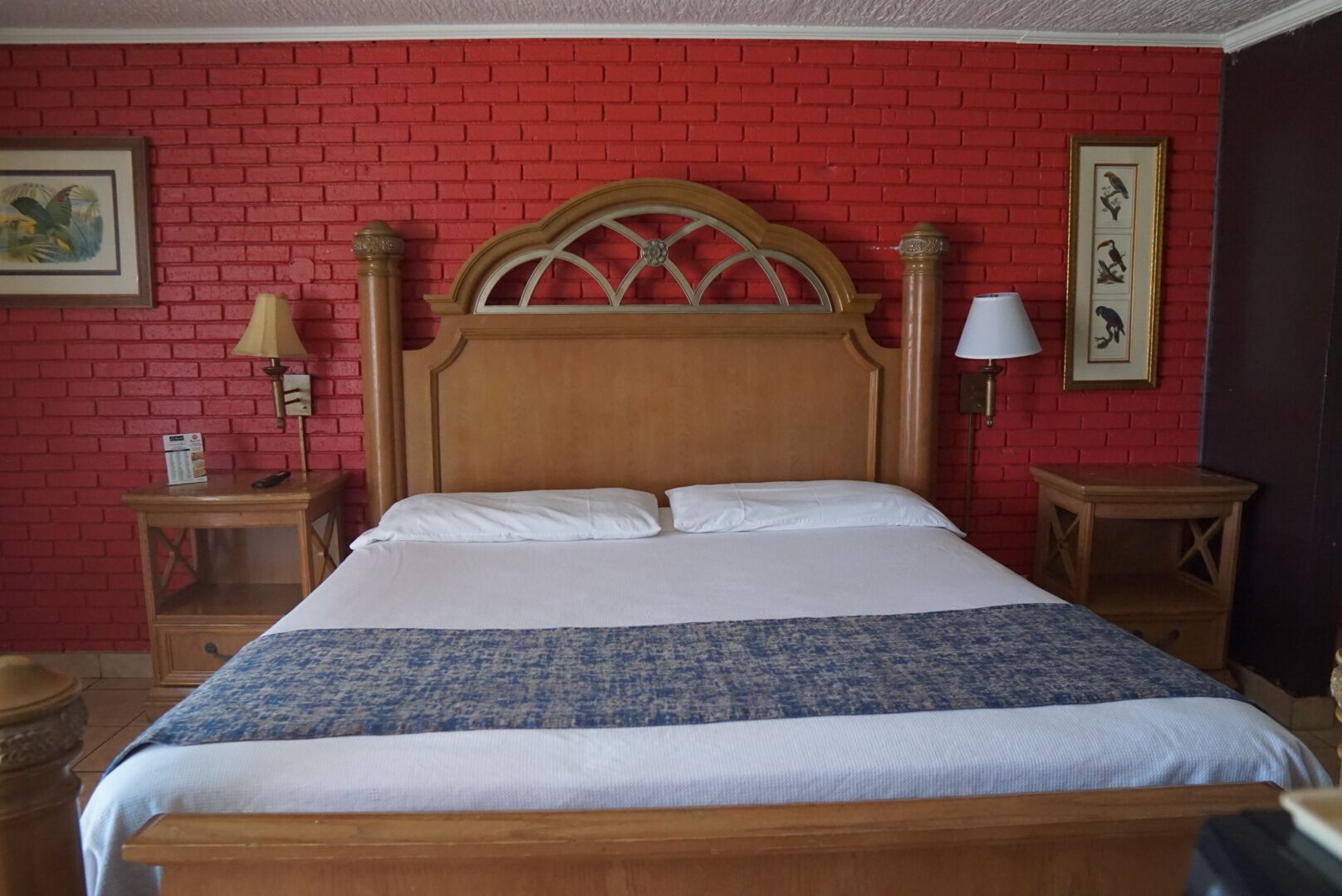 A bed with a wooden headboard, white bedding, and a blue patterned throw. There are two bedside tables with lamps and framed pictures on the wall.