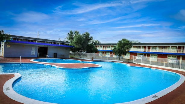 A swimming pool with a blue water feature, surrounded by a fenced area with a building in the background. - La Hacienda Hotel (Laredo)