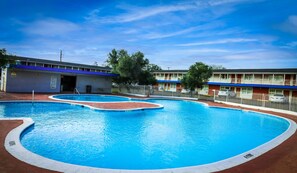 A swimming pool with a blue water feature, surrounded by a fenced area with a building in the background.