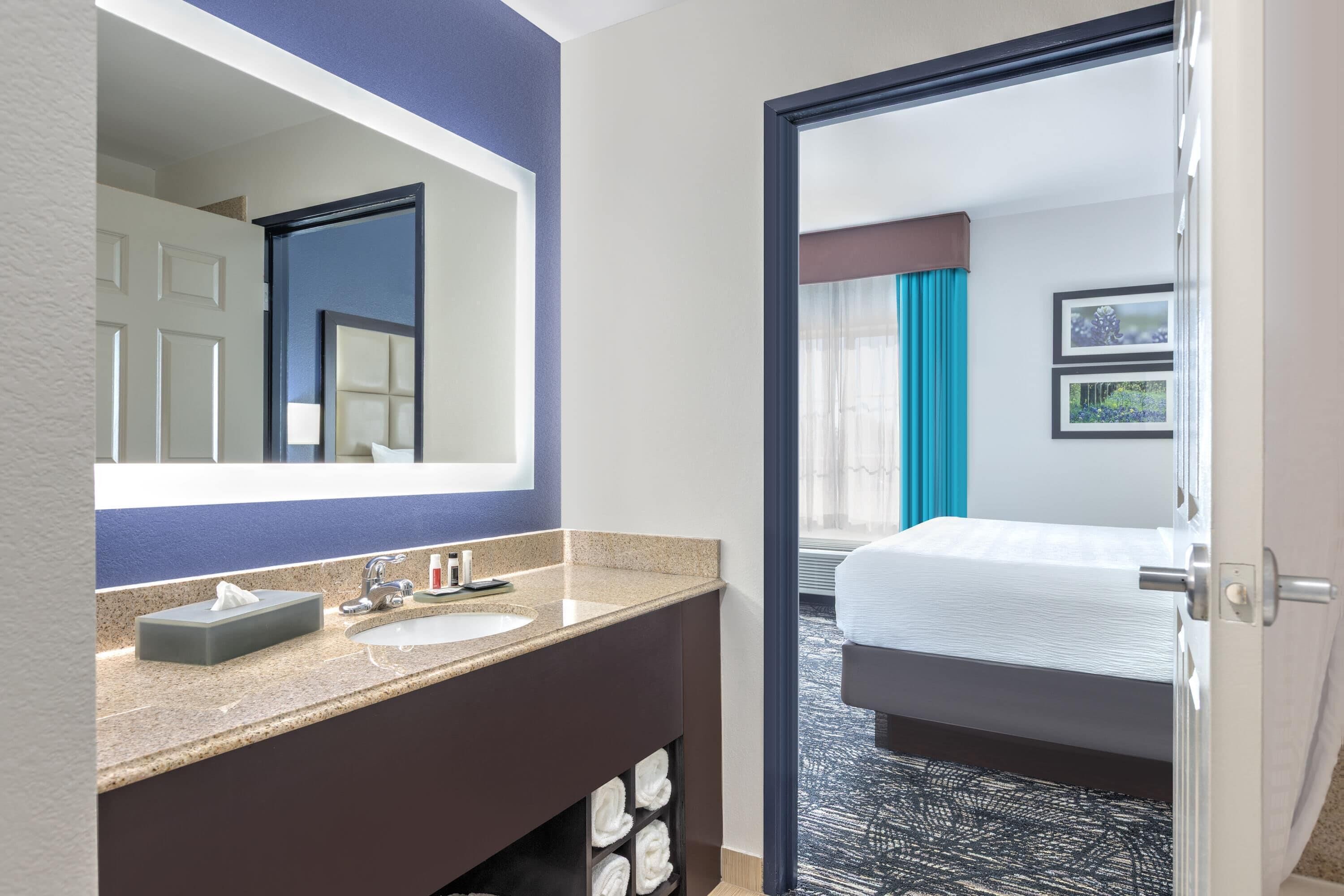 Habitación de hotel con baño que incluye un lavamanos, espejo y perchero.