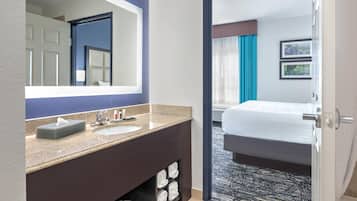 Habitación de hotel con baño que incluye un lavamanos, espejo y perchero.