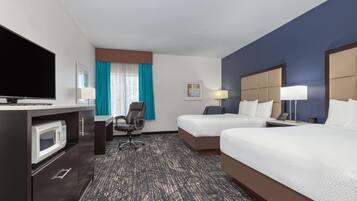 Habitación de hotel con dos camas, un escritorio con televisor, microondas, una silla y una ventana con cortinas.