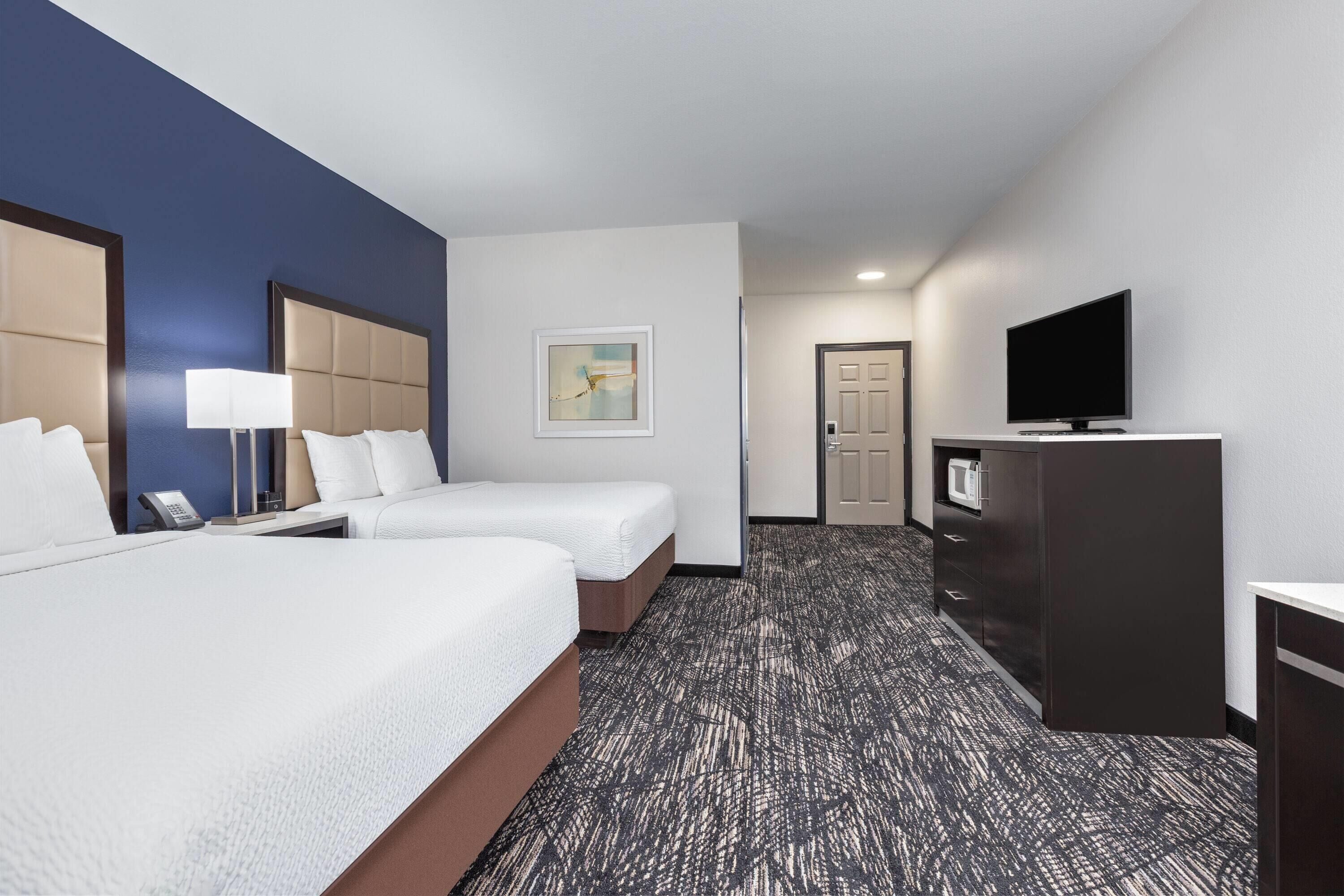A hotel room with two beds, a television, a desk, and a door.