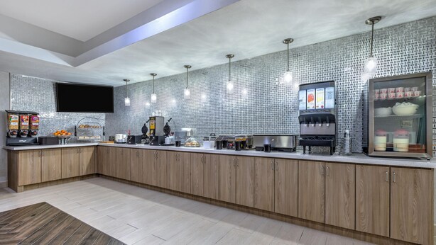 A modern kitchen with a long counter, wooden cabinets, a flat-screen TV, and a coffee machine. - La Quinta Inn & Suites by Wyndham Paris (Paris)