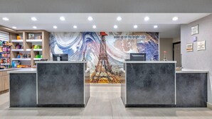 A hotel reception area with two reception desks, a large mural of the Eiffel Tower, and a variety of snacks and beverages on shelves. - La Quinta Inn & Suites by Wyndham Paris (Paris)